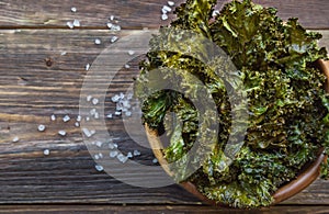 Homemade green kale chips in bowl on rustic wooden background