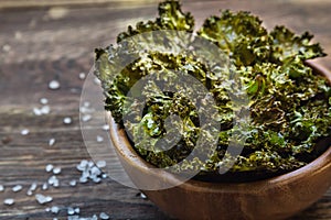 Homemade green kale chips in bowl on rustic wooden background