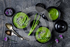 Homemade green spring asparagus cream soup decorated with black sesame seeds and edible chives flowers.