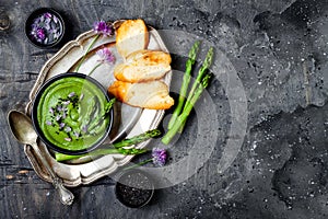 Homemade green spring asparagus cream soup decorated with black sesame seeds and edible chives flowers.