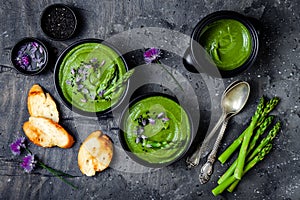 Homemade green spring asparagus cream soup decorated with black sesame seeds and edible chives flowers.