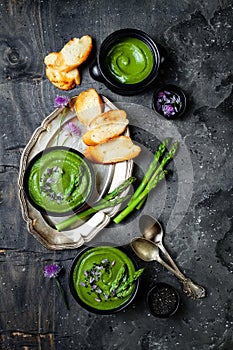 Homemade green spring asparagus cream soup decorated with black sesame seeds and edible chives flowers.