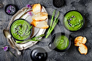 Homemade green spring asparagus cream soup decorated with black sesame seeds and edible chives flowers.