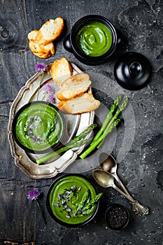 Homemade green spring asparagus cream soup decorated with black sesame seeds and edible chives flowers.