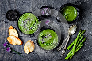 Homemade green spring asparagus cream soup decorated with black sesame seeds and edible chives flowers.