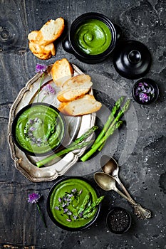 Homemade green spring asparagus cream soup decorated with black sesame seeds and edible chives flowers.