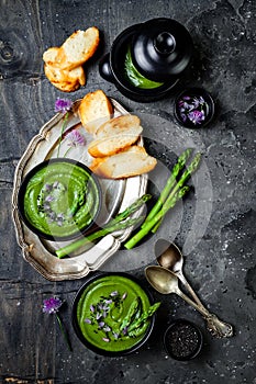 Homemade green spring asparagus cream soup decorated with black sesame seeds and edible chives flowers.