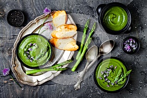 Homemade green spring asparagus cream soup decorated with black sesame seeds and edible chives flowers.