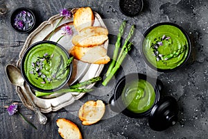 Homemade green spring asparagus cream soup decorated with black sesame seeds and edible chives flowers.