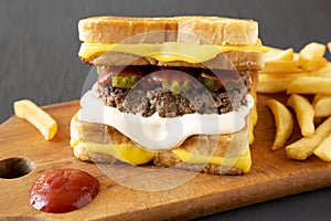 Homemade Grilled Cheese Burger with French Fries on a rustic wooden board on a black background, side view. Close-up