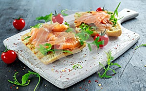 Homemade grilled toast with Smoked Salmon, rucola, tomatoes on white board. healthy breakfast