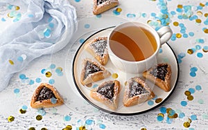 Homemade hamantashen cookies Haman`s ears with poppy seeds and apples in a festive atmosphere with confetti on a light gray