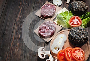 Homemade hamburger ingredients. Raw minced beef, fresh black bun, slice of cheese, tomato, onion rings, lettuce on wood