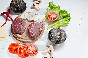 Homemade hamburger ingredients. Raw minced beef, fresh black bun, slice of cheese, tomato, onion rings, lettuce on wood
