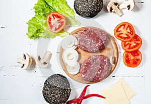 Homemade hamburger ingredients. Raw minced beef, fresh black bun, slice of cheese, tomato, onion rings, lettuce on wood white back