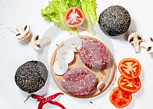 Homemade hamburger ingredients. Raw minced beef, fresh black bun, slice of cheese, tomato, onion rings, lettuce on wood white back