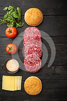 Homemade hamburger. Raw beef patties, sesame buns with other ingredients, on black wooden table background, top view flat lay,
