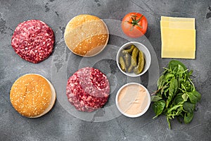 Homemade hamburger. Raw beef patties, sesame buns with other ingredients, on gray stone background, top view flat lay