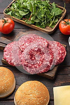 Homemade hamburger. Raw beef patties, sesame buns with other ingredients, on old dark  wooden table background