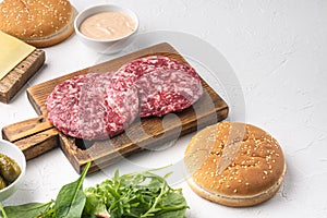 Homemade hamburger. Raw beef patties, sesame buns with other ingredients, on white stone  background, with copy space for text