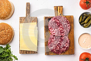 Homemade hamburger. Raw beef patties, sesame buns with other ingredients, on white stone  background, top view flat lay