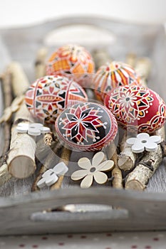 Homemade handmade painted Easter eggs on birch branches on grey wooden tray, traditional hnadcraft eggs, white flowers