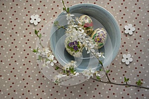 Homemade handmade painted Easter eggs in blue bowl on spotted tablecloth decorated with blackthorn sloe white flowering branch