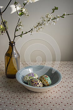 Homemade handmade painted Easter eggs in decorative light blue color bowl on wooden table, springtime flowering branches