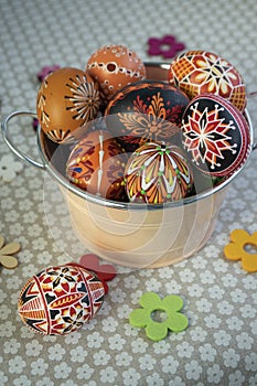 Homemade handmade painted Easter eggs in decorative old pink color tin on flowered tablecloth with decorative flowers