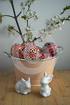 Homemade handmade painted Easter eggs in decorative old pink color tin on wooden table, springtime flowering branches