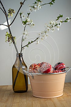 Homemade handmade painted Easter eggs in decorative old pink color tin on wooden table, springtime flowering branches