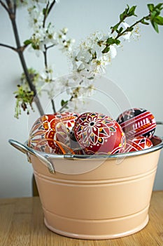 Homemade handmade painted Easter eggs in decorative old pink color tin on wooden table, springtime flowering branches