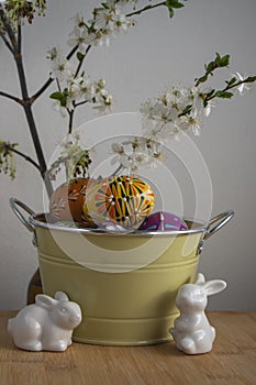 Homemade handmade painted Easter eggs in decorative old pink color tin on wooden table, springtime flowering branches