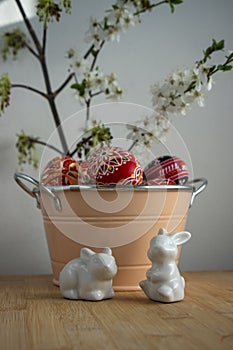 Homemade handmade painted Easter eggs in decorative old pink color tin on wooden table, springtime flowering branches