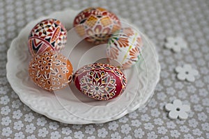 Homemade handmade painted Easter eggs on white plate dish on tablecloth with white petal flowers, Eastertime decoration