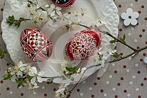 Homemade handmade painted Easter eggs on white plate on spotted tablecloth decorated with blackthorn sloe white flowering branch