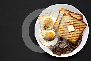 Homemade Healthy Sunnyside Eggs Breakfast on a white plate on a black surface, top view. Flat lay, overhead, from above. Copy