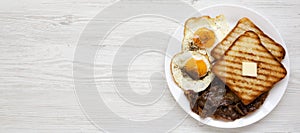 Homemade Healthy Sunnyside Eggs Breakfast on a white plate on a white wooden surface, top view. Flat lay, overhead, from above.