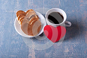 Homemade heart shaped pancakes on a white plate, a mug with coffee or cocoa and a red blank heart shape