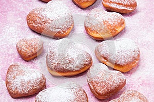 Homemade heart sheped donuts with powdered sugar on pnk background.