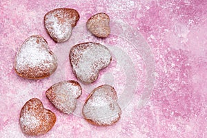 Homemade heart sheped donuts with powdered sugar on pnk background.
