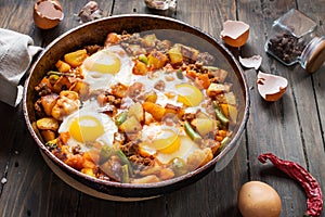 Homemade Hearty Breakfast Skillet with Eggs Potatoes and minced meat on wooden table