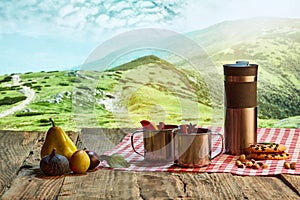 Homemade herbal or fruit tea. Glass pot, cup and sweets on wooden table over natural landscape background. Beauty, art