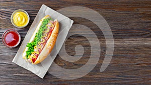 Homemade Hot Dog with mustard, ketchup, tomato and fresh salad leaves on brown wooden background