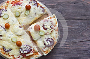 Homemade hot pizza with salami and cheese, pickles and tomatoes on wooden background, ready to eat
