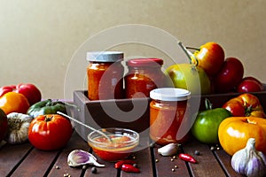 Homemade hot tomato sauce adjika in jars - Tomatoes, chilli pepper, garlic, herbs on wooden table.