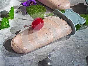 Homemade ice cream of fruit and cream on decorative skewers is on a light background. The composition is decorated with pieces of