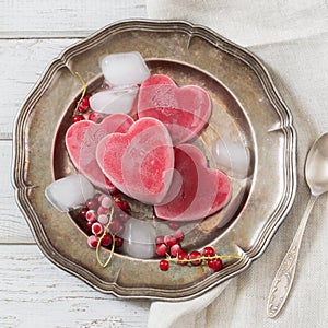 Homemade ice cream of red currant in shape of heart and on vintage dish and wooden background. Top view. Frozen drinks.