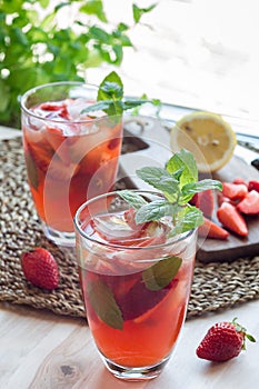 Homemade iced tea with strawberries and mint on wooden table, vertical