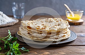 Homemade Indian flat bread Chapati or Roti on wooden background with butter ghee, flour, water and cilantro